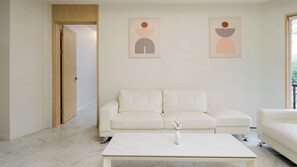 Una sala de estar minimalista con un sofá blanco, una mesita de centro y dos obras de arte abstracto en la pared.