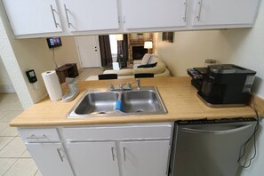 Una cocina compacta con un lavamanos de acero inoxidable, una cafetera y un refrigerador.