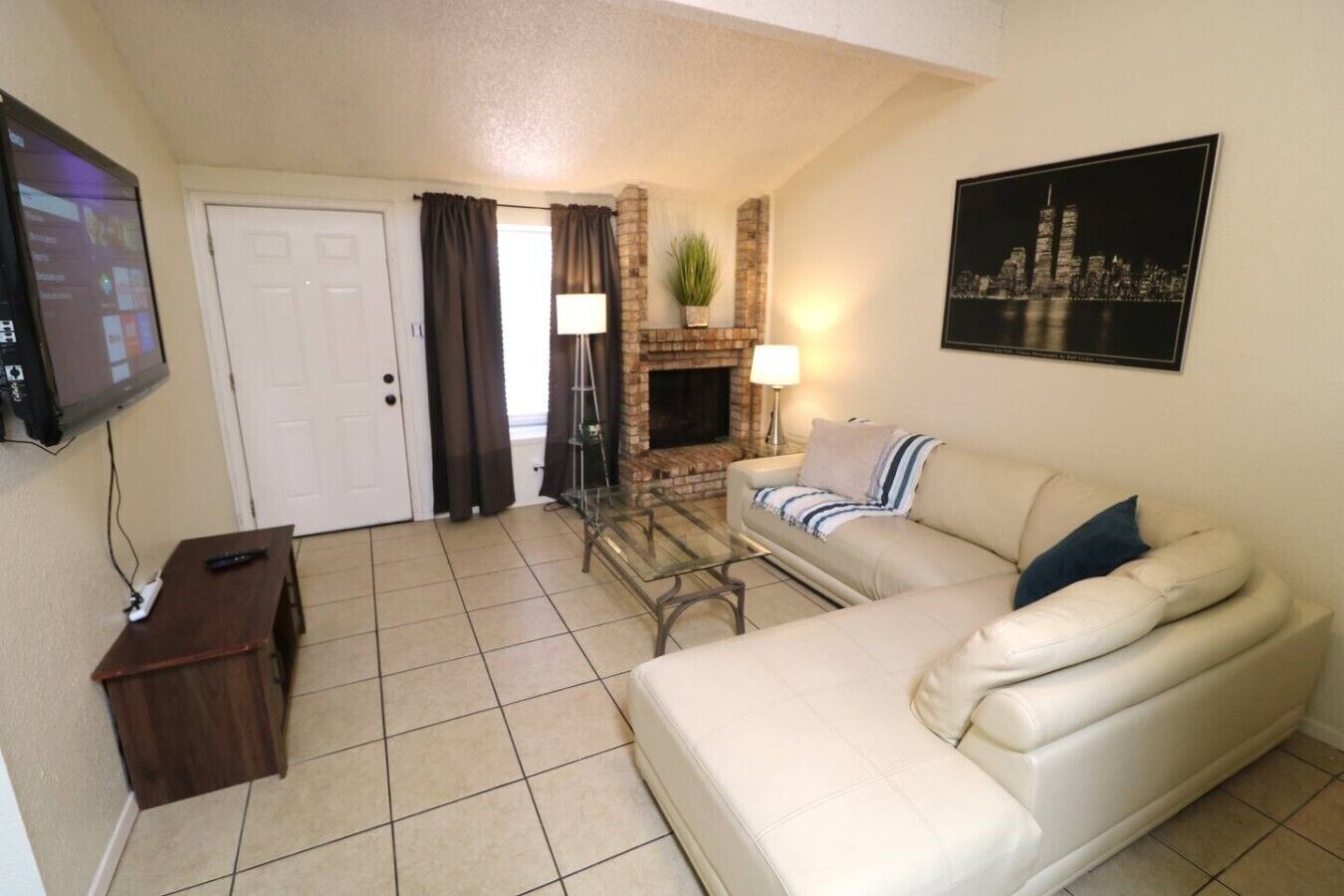 A living room with a sofa, a TV, a fireplace, and a cityscape painting.