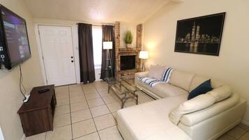 A living room with a sofa, a TV, a fireplace, and a cityscape painting.