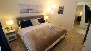Ein Hotelzimmer mit Bett, Nachttischen, einer Lampe, Wandbildern und einem Fernseher.