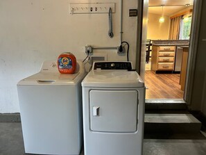 Deux machines à laver superposées dans un espace buanderie, avec une prise de courant visible, et une cuisine en arrière-plan.