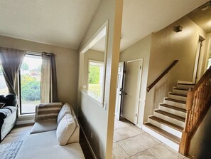 Un salon avec un canapé, une fenêtre avec des rideaux, un escalier et une porte donnant sur une autre pièce.