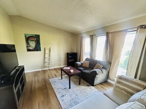 Un salon avec un canapé, une table basse, un téléviseur, une bibliothÚque et un tableau accroché au mur.