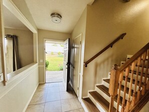 A hallway with a wooden staircase, a door leading outside, and a ceiling light fixture.