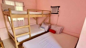 Habitación con literas, ventana y aire acondicionado, con un almohadón rojo.