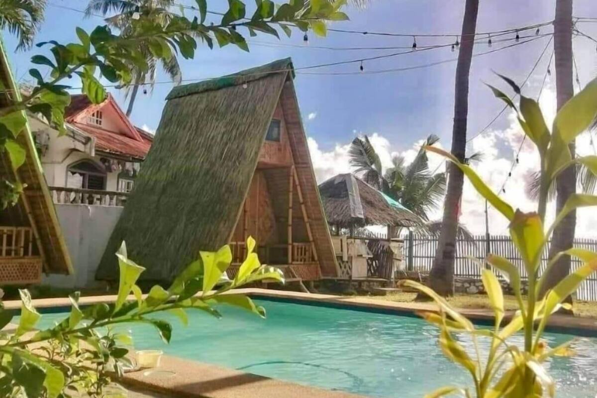 A pool area with a thatched-roof structure, palm trees, and a building with a red roof.