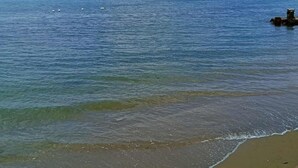 Una playa con aguas cristalinas, una orilla arenosa y un promontorio rocoso.