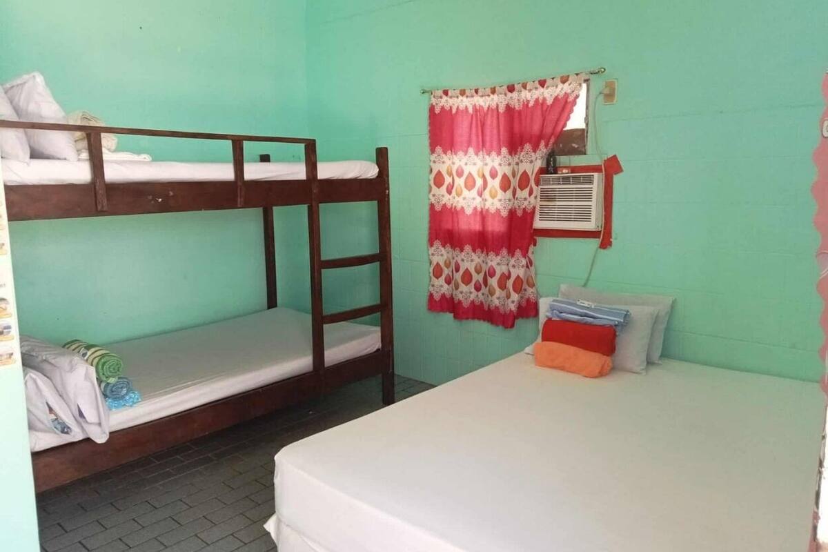A dormitory room with bunk beds, a single bed, a window with a curtain, and a wall-mounted air conditioning unit.