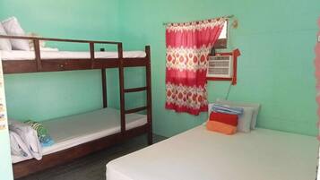 A dormitory room with bunk beds, a single bed, a window with a curtain, and a wall-mounted air conditioning unit.