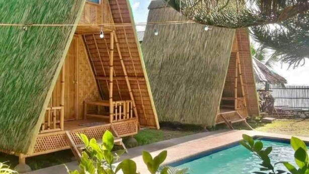 Un área junto a la piscina con cabañas de techo de paja, una piscina cristalina y abundante vegetación.