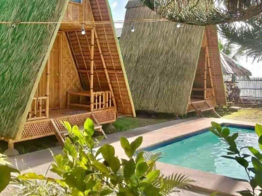 A poolside area with thatched-roof huts, a clear pool, and surrounding greenery.