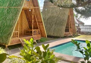 A poolside area with thatched-roof huts, a clear pool, and surrounding greenery.