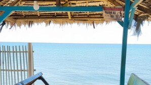 Una estructura frente al mar con techo de paja, un cartel que indica una zona para nadar y vistas al océano.