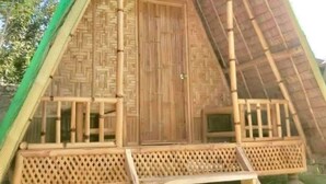 Una estructura triangular con puerta de madera, un balcón con celosía y techo de paja.