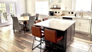 A modern kitchen with a central island, dining area with wicker chairs, and a ceiling fan. - Spacious Lake Lanier property - Close to Atlanta and full of amenities (Buford)