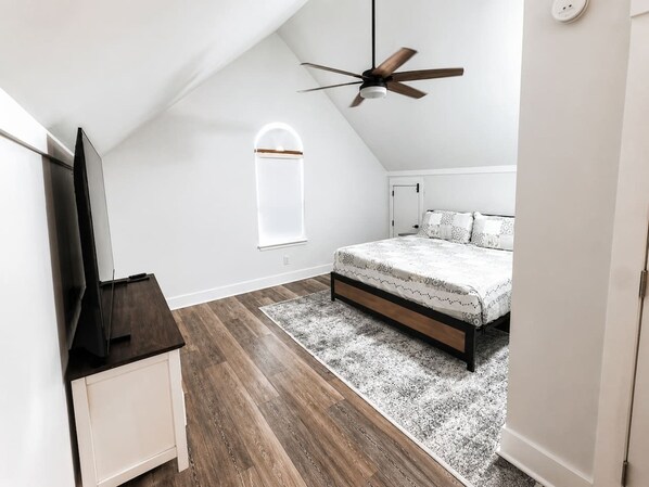 A bedroom with a bed, a ceiling fan, a TV, and a window.