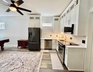 A modern kitchen with white cabinets, stainless steel appliances, and a ceiling fan.