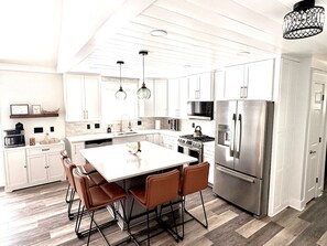 A modern kitchen with white cabinetry, stainless steel appliances, and a central island with seating.