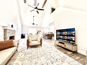 A living room with a fireplace, a sofa, a coffee table, a TV, and a ceiling fan.