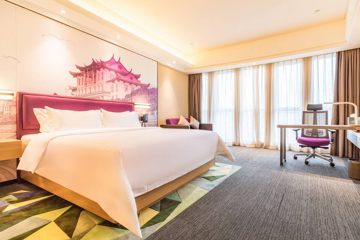 Ein Hotelzimmer mit einem großen Bett, einem Schreibtisch, einem Stuhl und einem Fenster mit Vorhängen.