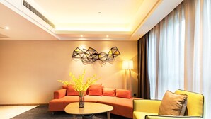 A modern hotel room with a sofa, a yellow armchair, a round table with a vase, and geometric wall art. - Hampton by Hillton Xiamen City Plaze (Xiamen)
