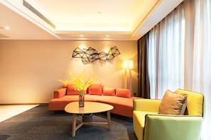 Ein modernes Hotelzimmer mit einer Couch, einem gelben Sessel, einem runden Tisch mit einer Vase und geometrischer Wandkunst.