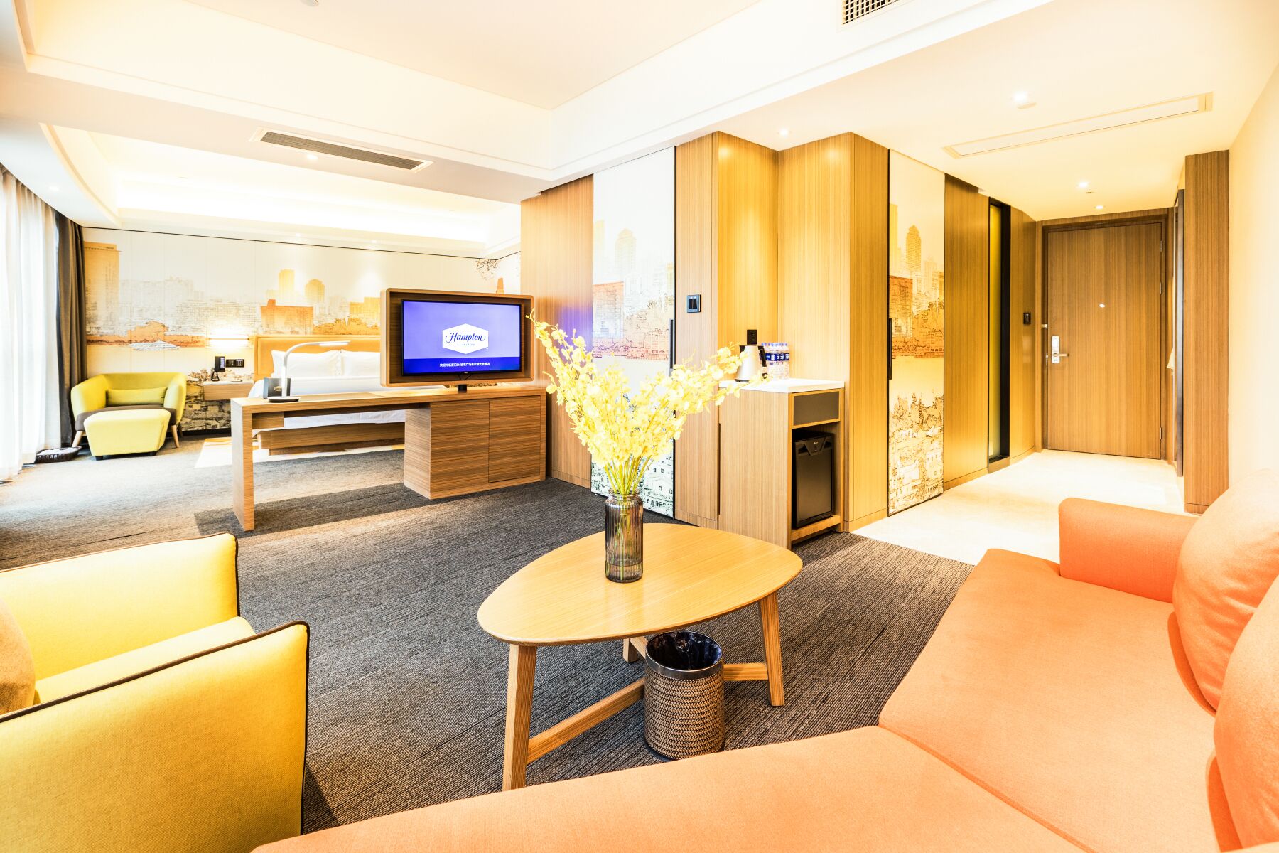 Quarto de hotel com televisão, sofá, mesa de centro e escrivaninha com computador.