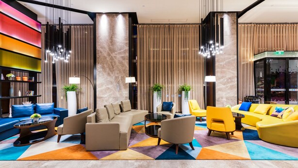 A modern lobby with a sectional sofa, armchairs, a coffee table, and a bookshelf. - Hampton by Hillton Xiamen City Plaze (Xiamen)