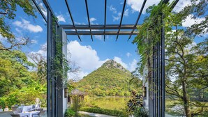 An outdoor dining area with tables and chairs, a pergola structure, and a view of a mountain and lake. - Guilin Heshe Lakeside Resort (Guilin)