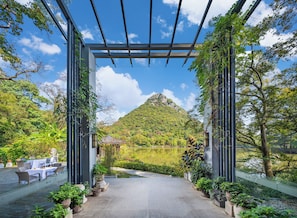 An outdoor dining area with tables and chairs, a pergola structure, and a view of a mountain and lake.