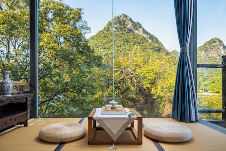 A room with tatami flooring, a low wooden table with a white cloth, and a view of a mountainous landscape.