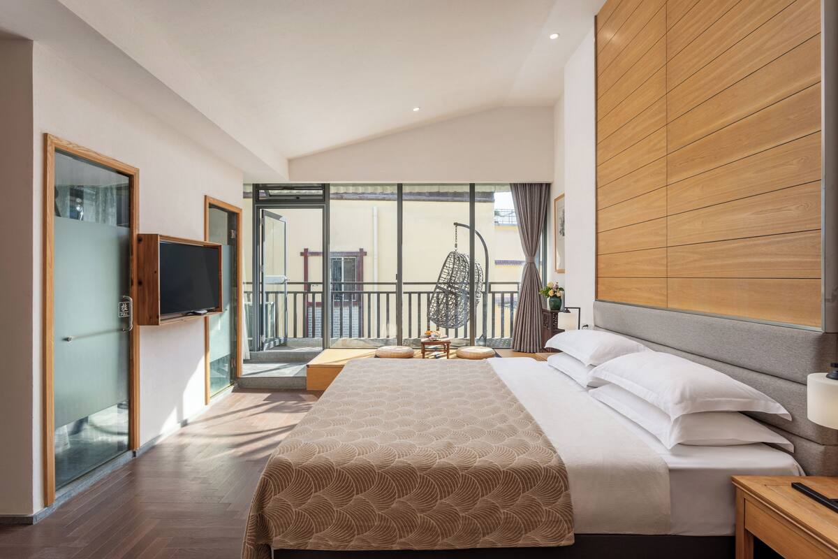 A hotel room with a bed, a TV, a balcony with a chair, and a wooden wall.