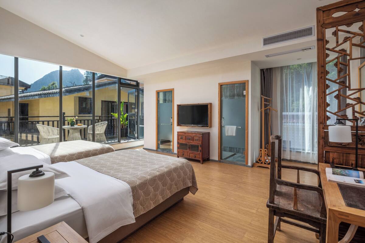 A hotel room with a balcony, a bed, a desk, a TV, and a wardrobe.