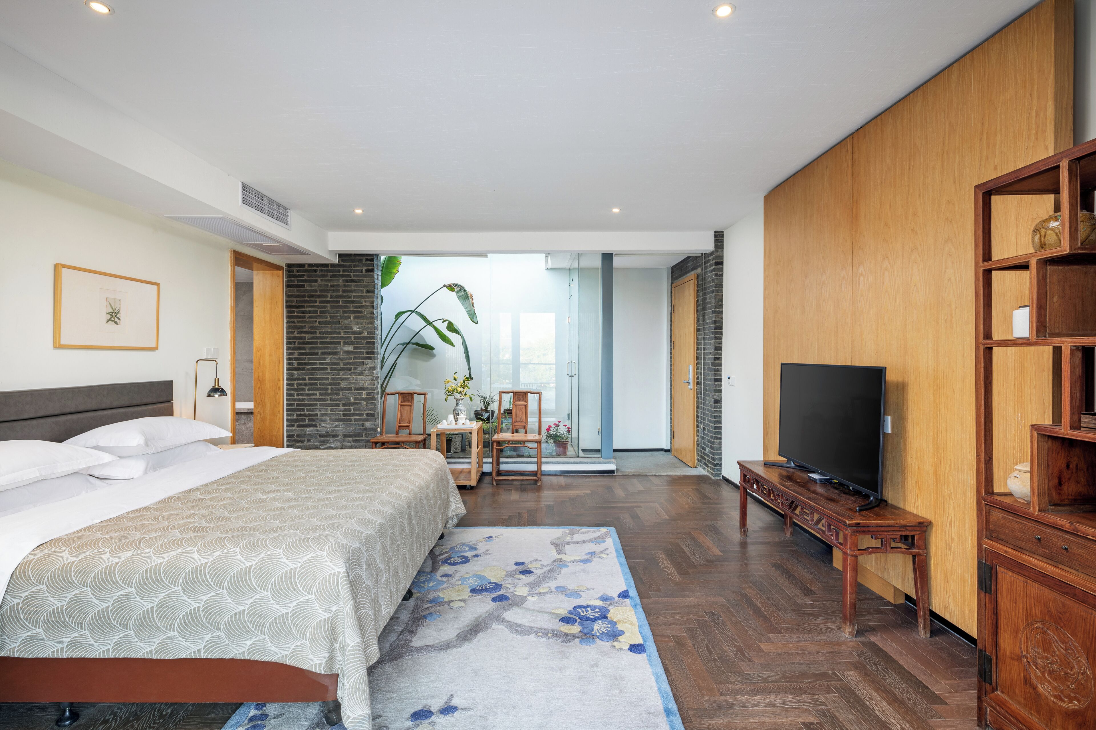 Una habitación de hotel moderna con una cama grande, televisión, una estantería de madera y vistas al exterior.