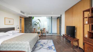 Una habitación de hotel moderna con una cama grande, televisión, una estantería de madera y vistas al exterior.