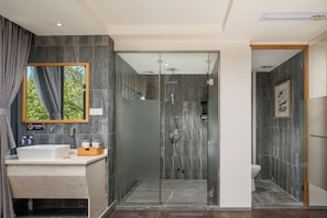 Ein modernes Badezimmer mit einer begehbaren Glasdusche, einem Waschbecken mit Marmorplatte und einem großen Spiegel.