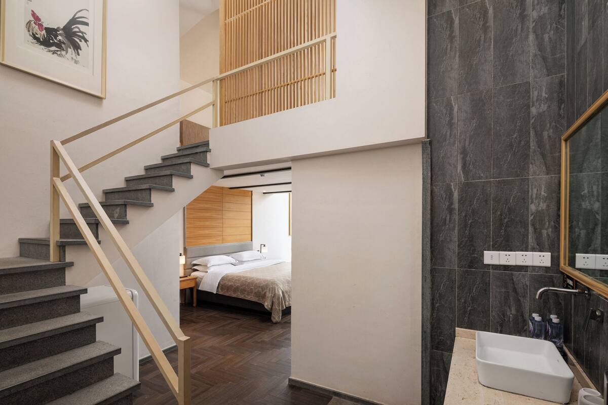 A modern interior with a staircase leading to a bedroom, a bathroom with a large mirror, and a wooden ceiling.