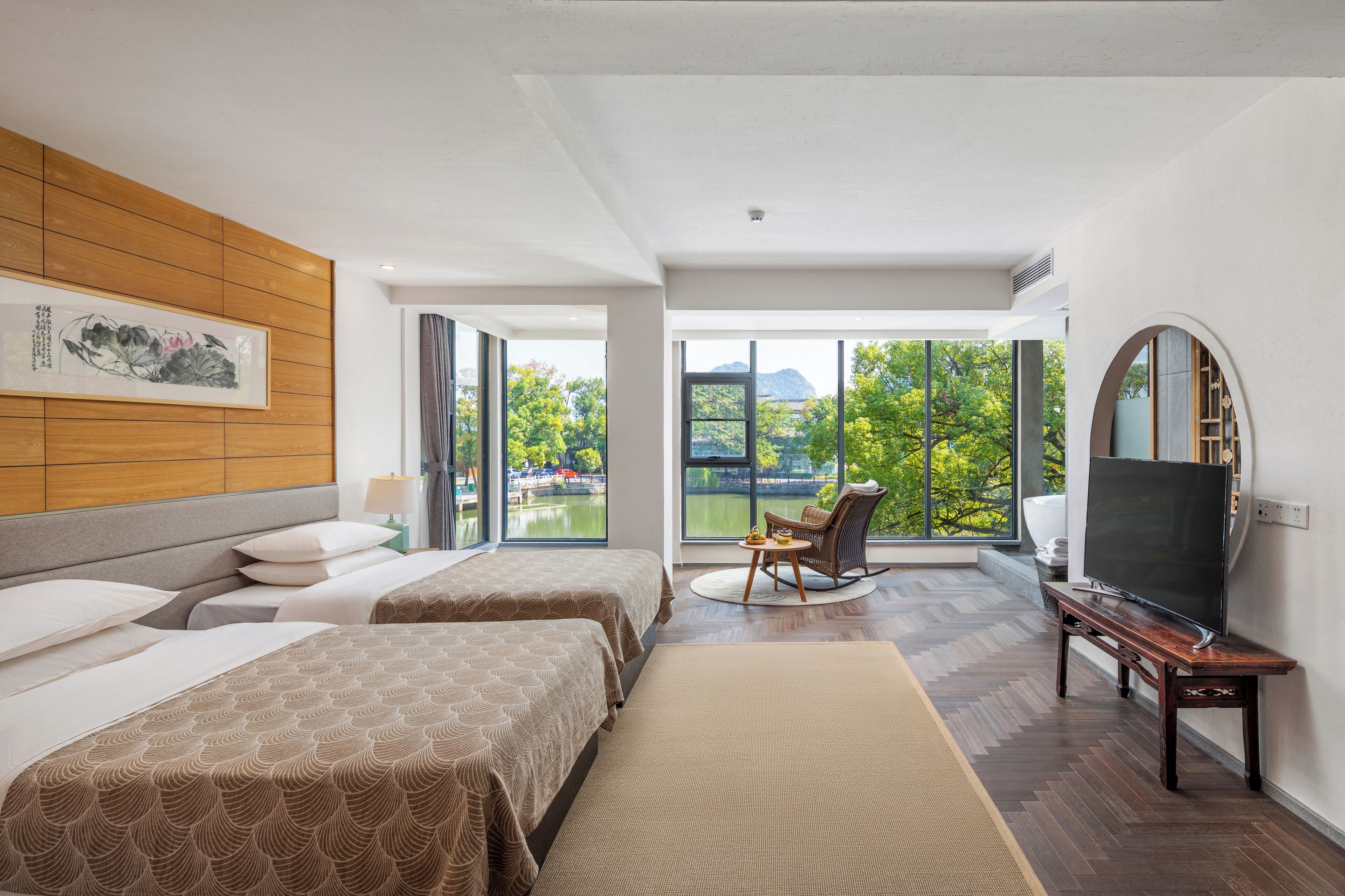 A hotel room with two beds, a TV, a chair, and a large window with a view of greenery.