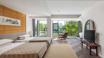 A hotel room with two beds, a TV, a chair, and a large window with a view of greenery.