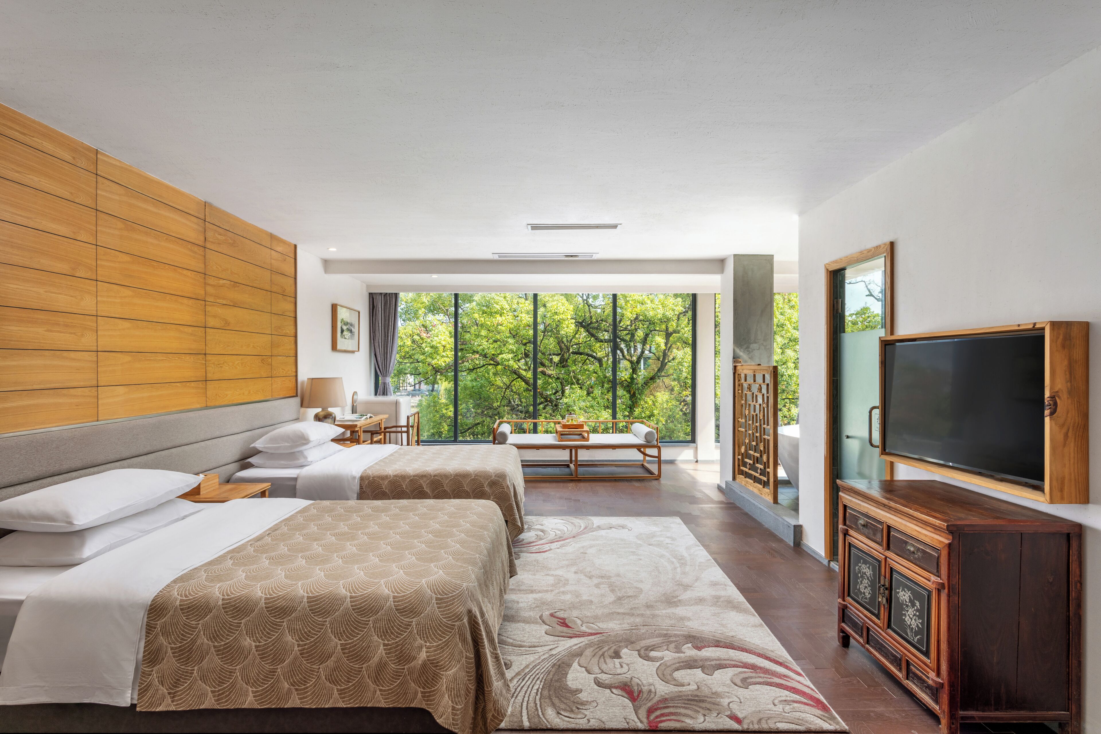 A hotel room with two beds, a large window, a TV, and a wooden cabinet.