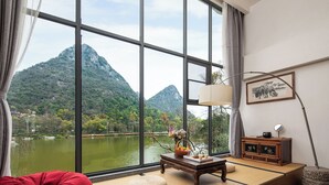A room with a large window, a wooden table with a basket, a red cushion, and a traditional Japanese-style sofa. - Guilin Heshe Lakeside Resort (Guilin)