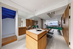 Una cocina moderna con una isla central, un comedor con mesa y sillas, y vistas de la ciudad a través de amplios ventanales.