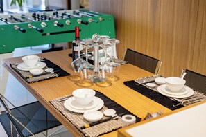 A dining table set with white dishes, glasses, and chopsticks, with a green foosball table in the background. - Chengyu B&B-Loft view suite (Zhangjiajie)