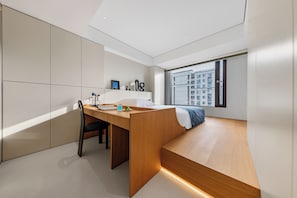 A modern bedroom with a built-in desk, a bed, and a large window offering a city view.