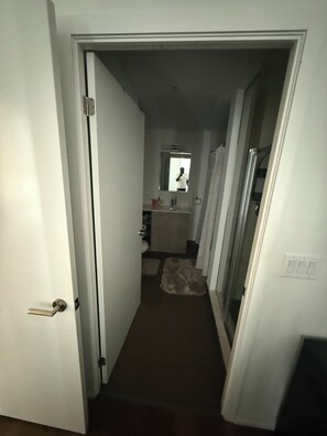 Un pasillo estrecho que conduce a un baño con espejo, lavabo e inodoro.