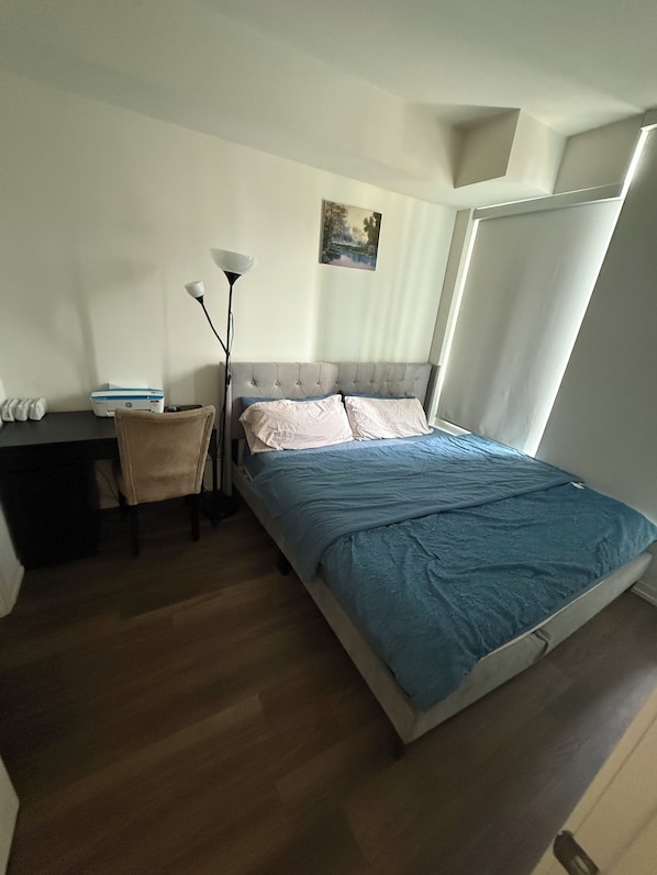 Une chambre à coucher avec un lit, un bureau, une chaise, une lampe sur pied et un tableau accroché au mur.