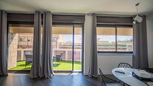 A room with a sliding glass door leading to a balcony with a view of a building and a fenced yard. There is a table with chairs and a remote control on it. - Newhouse ARGIRO Deluxe (Bari)