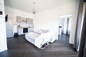 A modern hotel room with a bed, a kitchenette, and a bathroom.