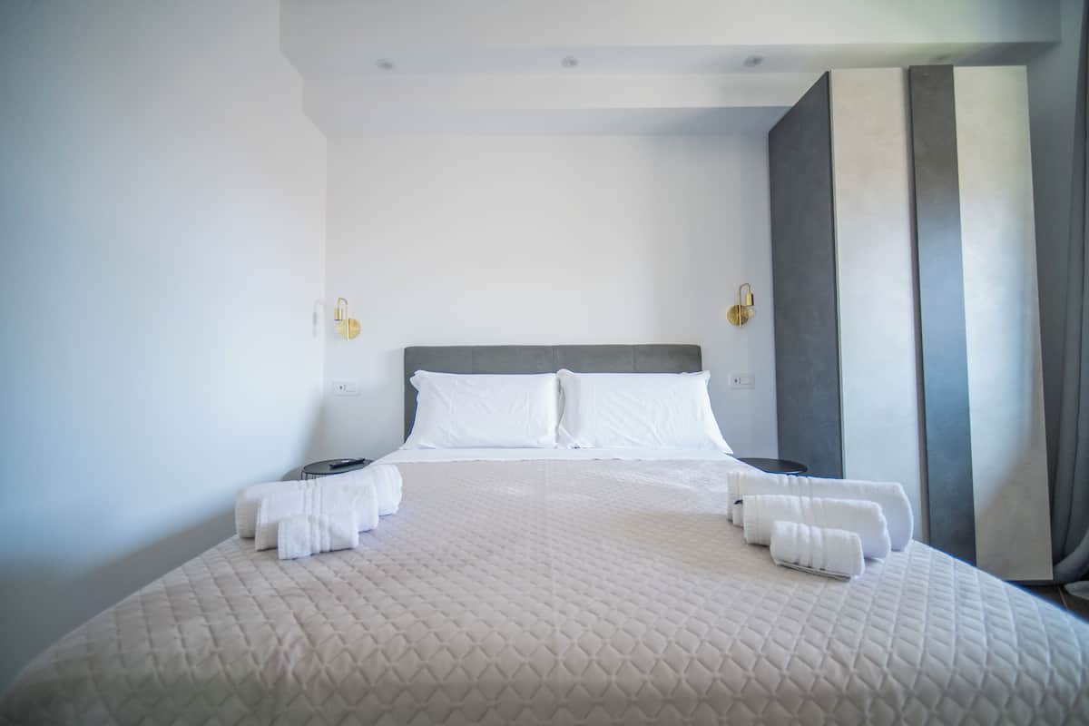 A neatly made bed with white linens, a grey headboard, and two bedside lamps.